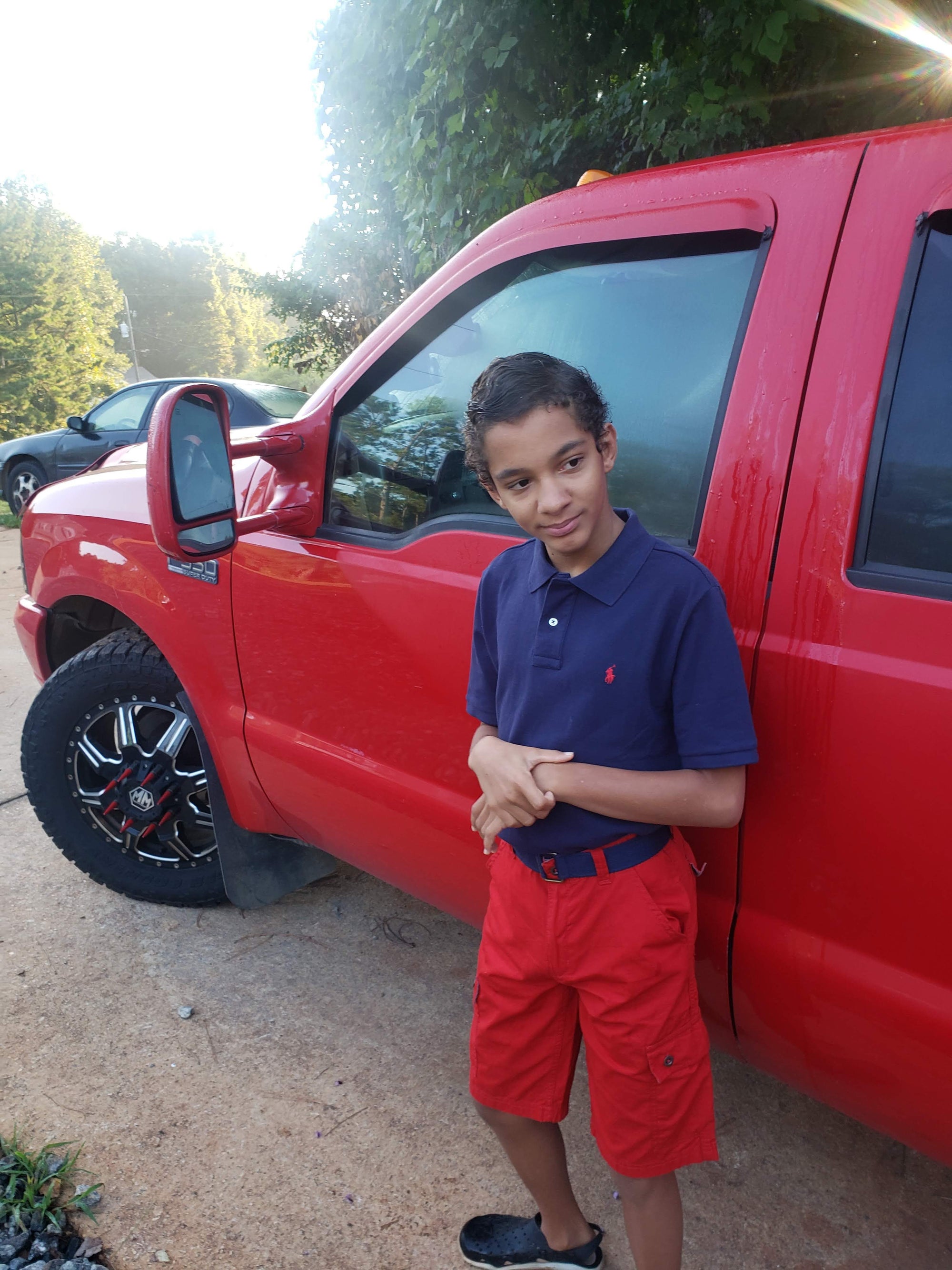 a Young nonverbal boy standing next to a red truck outdoors